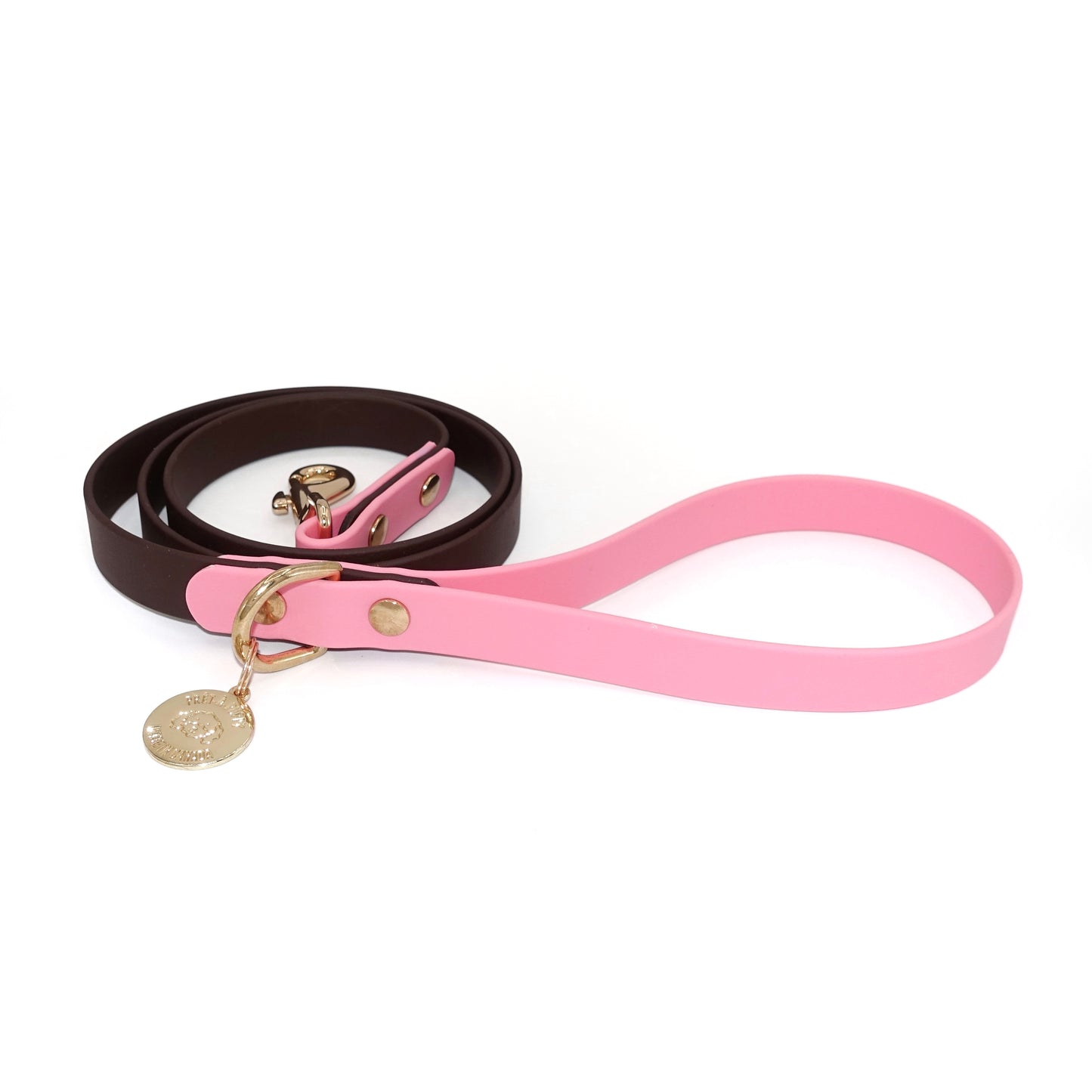 Dog leash with a pink handle and dark brown body with gold hardware on a white background