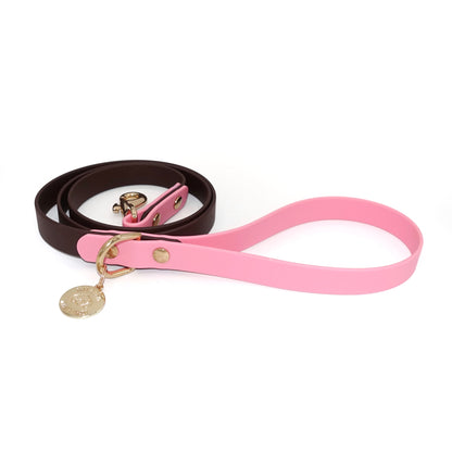 Dog leash with a pink handle and dark brown body with gold hardware on a white background