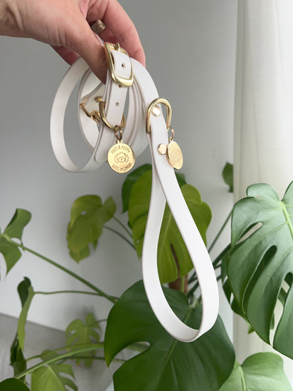 Stylish white dog leash made from soft, waterproof vegan leather, featuring durable shiny gold hardware, including a buckle and D-ring. Adorned with an elegant charm, this leash combines functionality and fashion, making it perfect for the modern pet owner.